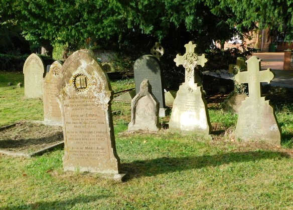 Colour photo of part of the churchyard at Waters Upton St Michael, showing seven gravestones in various styles and sizes.